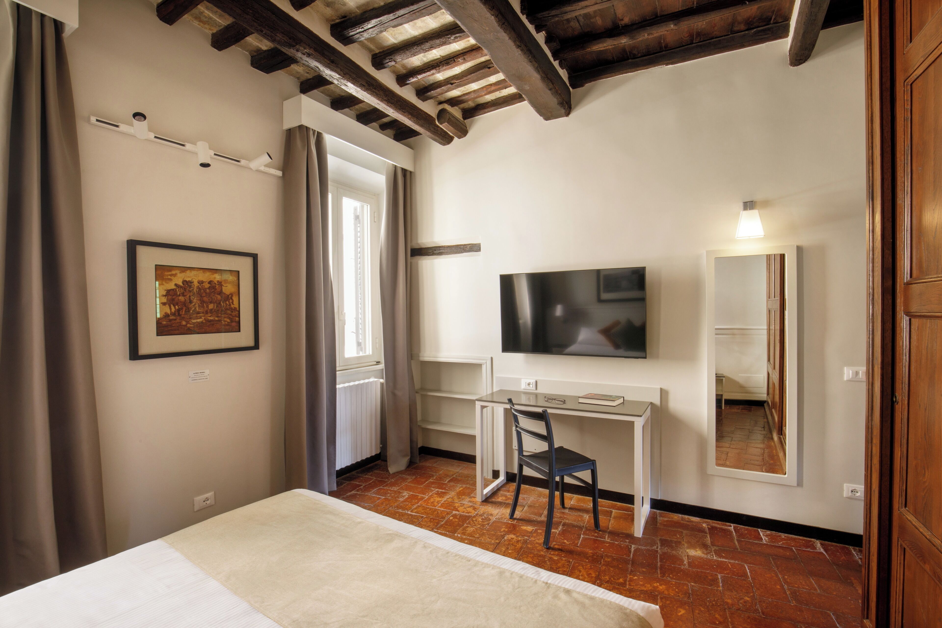 A bedroom with a bed, a desk, a chair, a TV, and a mirror.
