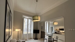 A modern living room with a sofa, dining table, and chairs. There is a kitchen visible through an open doorway. - Aenea Superior Inn (Rome)