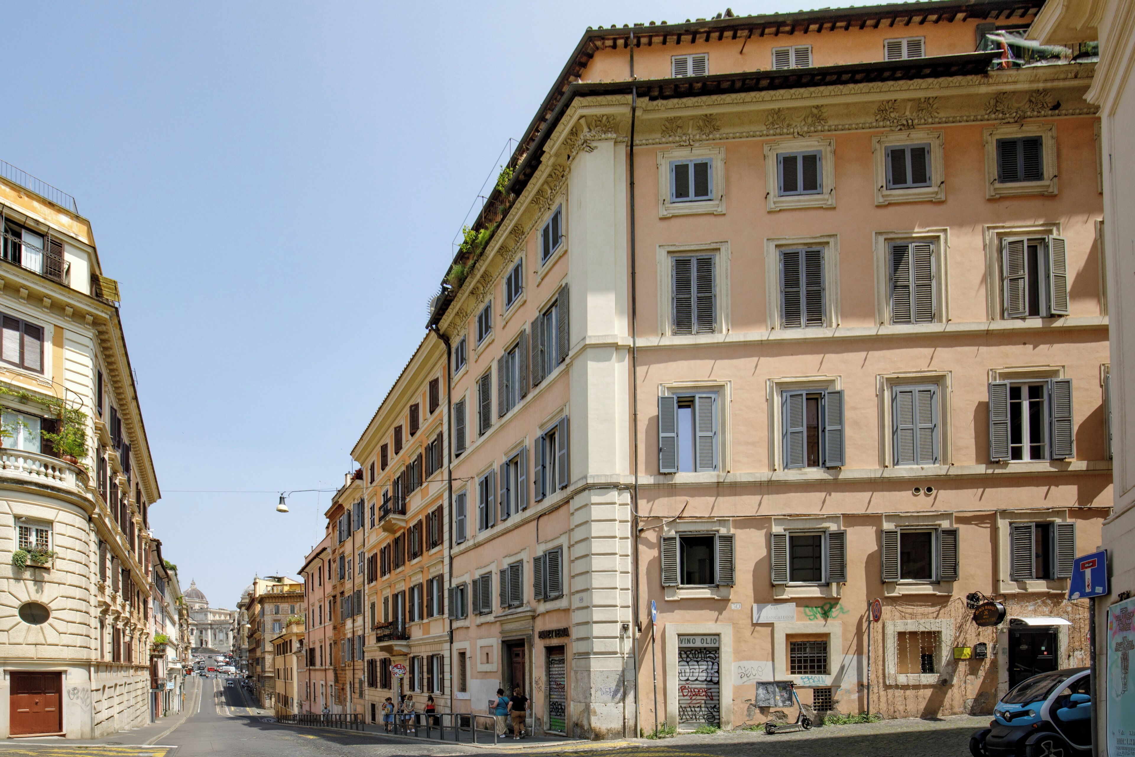 A street view of a building with multiple windows and balconies, a clear sky, and a few parked cars.