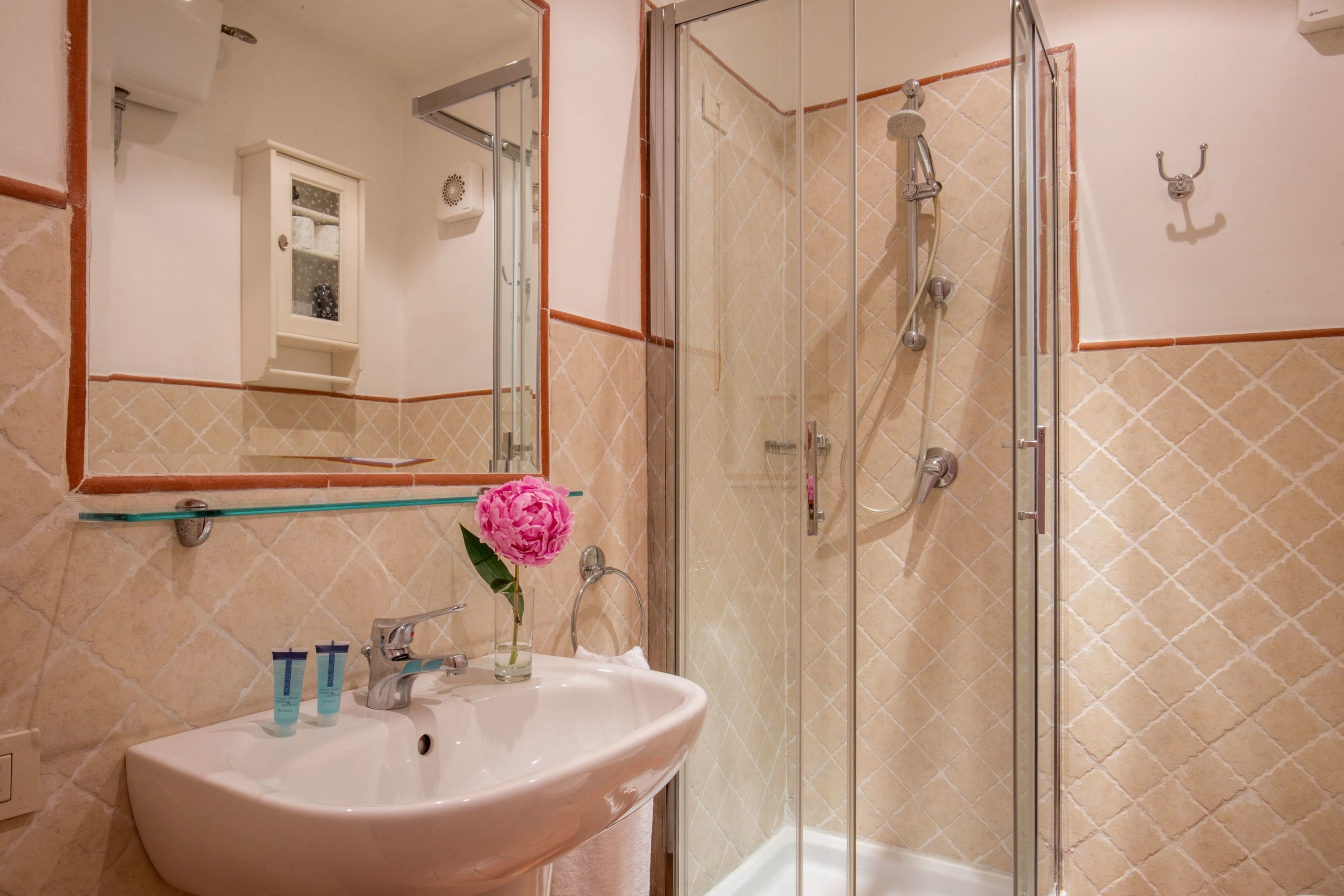 Un baño con cabina de ducha de vidrio, un lavabo con un florero y un espejo sobre el lavabo.