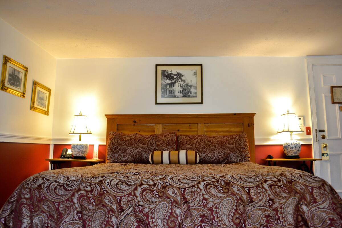 A bedroom with a large bed, two bedside tables, a wooden headboard, and framed pictures on the walls.