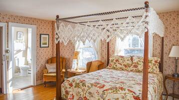 Een slaapkamer met een hemelbed, bloemenbehang en een houten vloer.