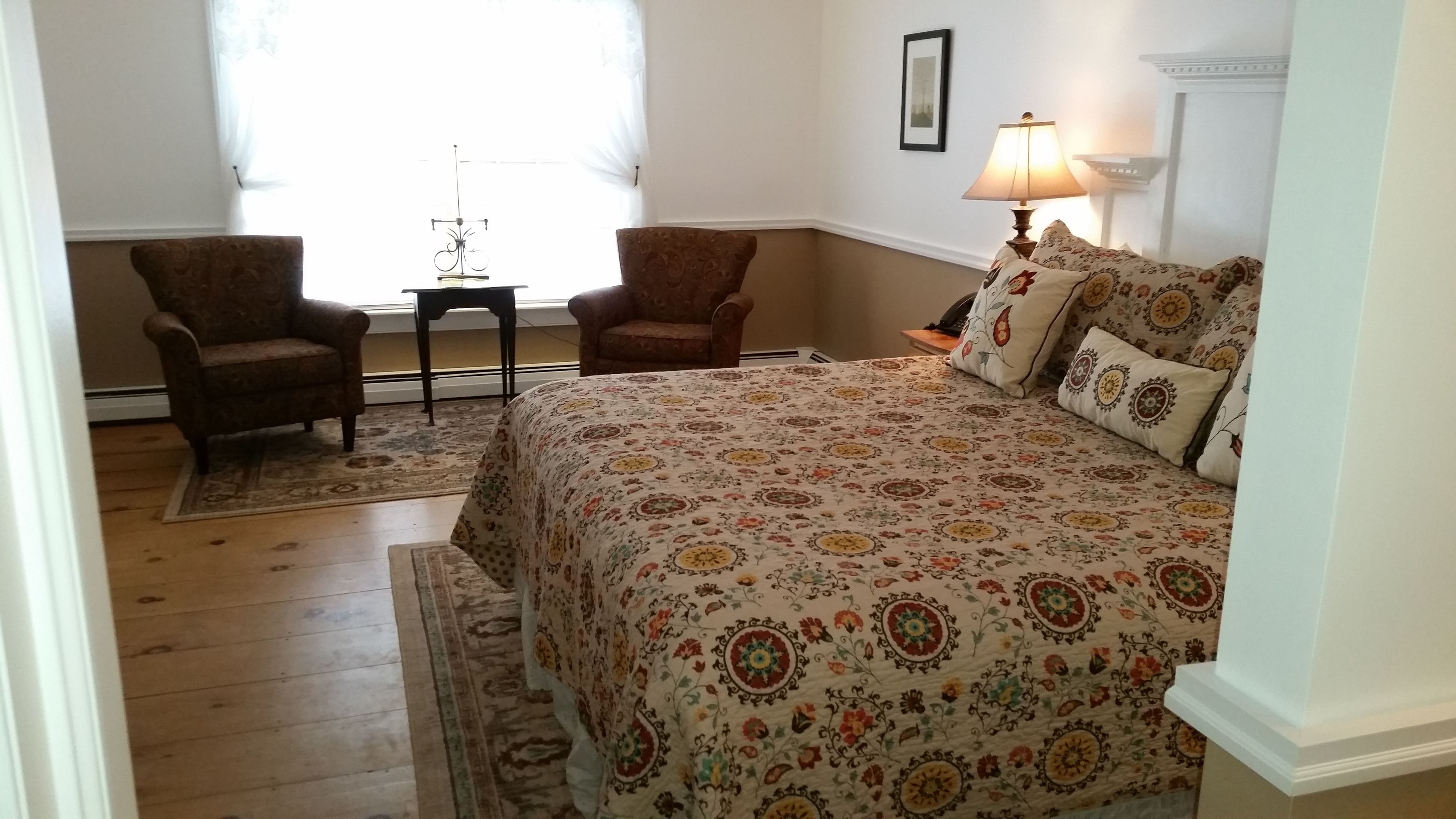 Un dormitorio con una cama grande, dos sillones, una mesita y una lámpara.