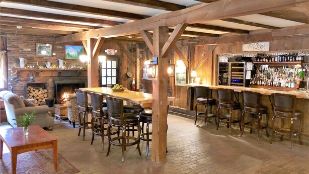 Un intérieur rustique comprenant un coin bar, des poutres en bois, une cheminée et une table à manger avec des chaises.