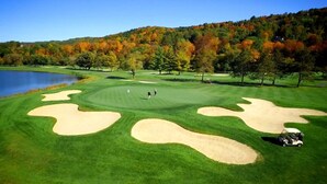 Un parcours de golf avec des bunkers de sable, un lac et, en arrière-plan, des arbres aux couleurs automnales.