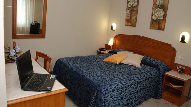 A bedroom with a bed, a desk with a laptop, a mirror, and two wall-mounted lamps. - Hotel Marzia (Scandicci)