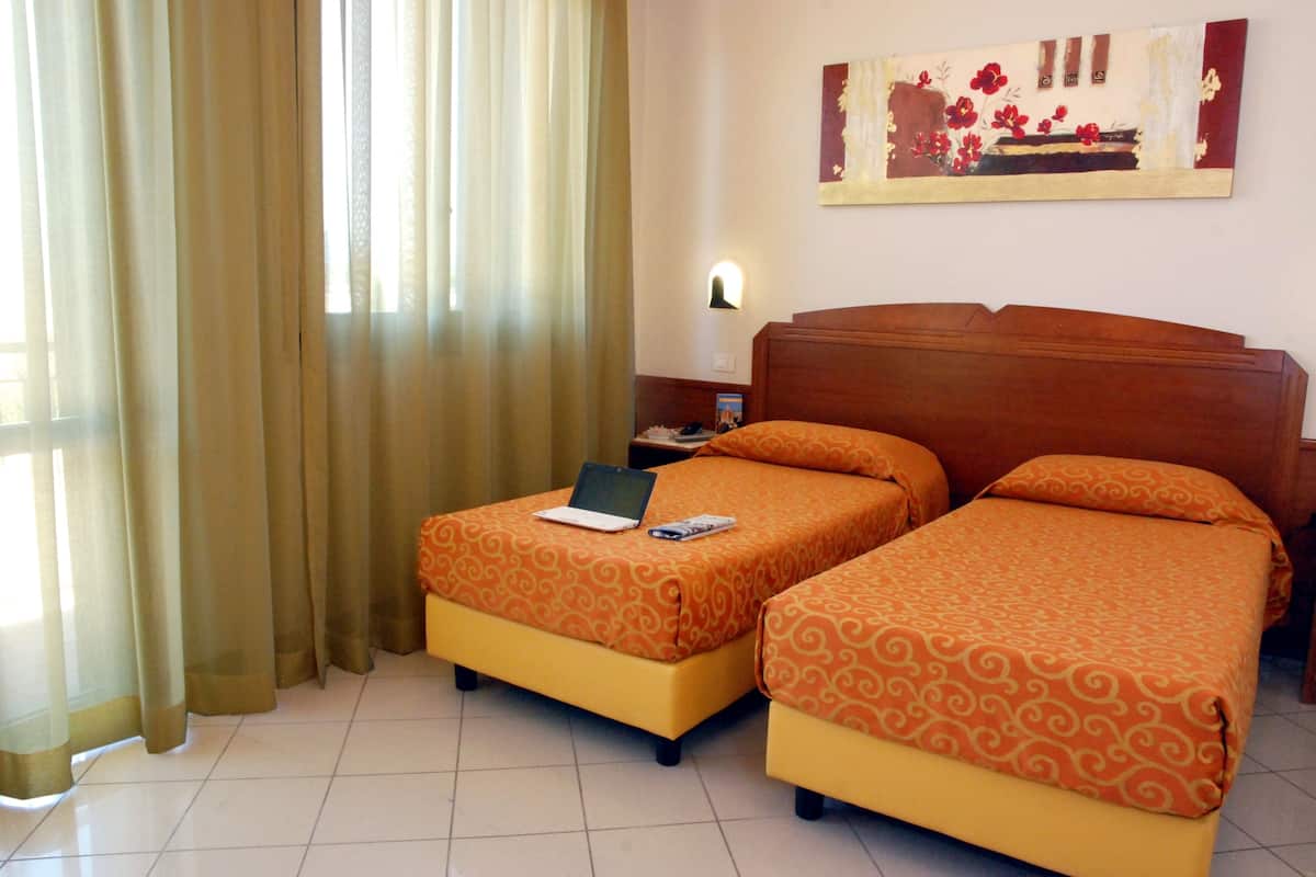 A hotel room with two single beds, a laptop on one bed, and a painting on the wall.