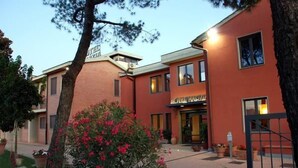 A hotel with a red facade, multiple windows, and a well-maintained garden with flowering plants. - Hotel Marzia (Scandicci)
