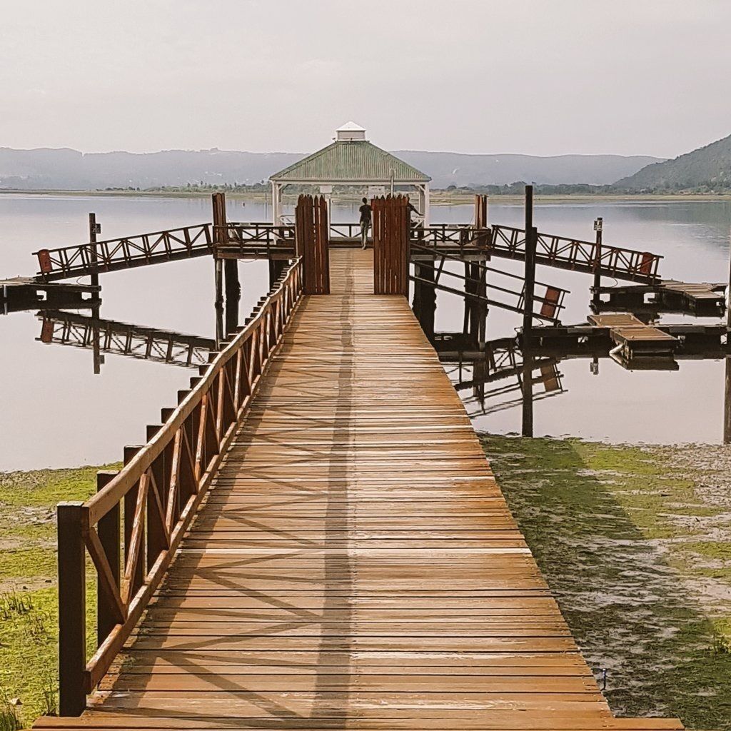 A wooden pier leading to a gazebo by a calm lake with mountains in the background.
