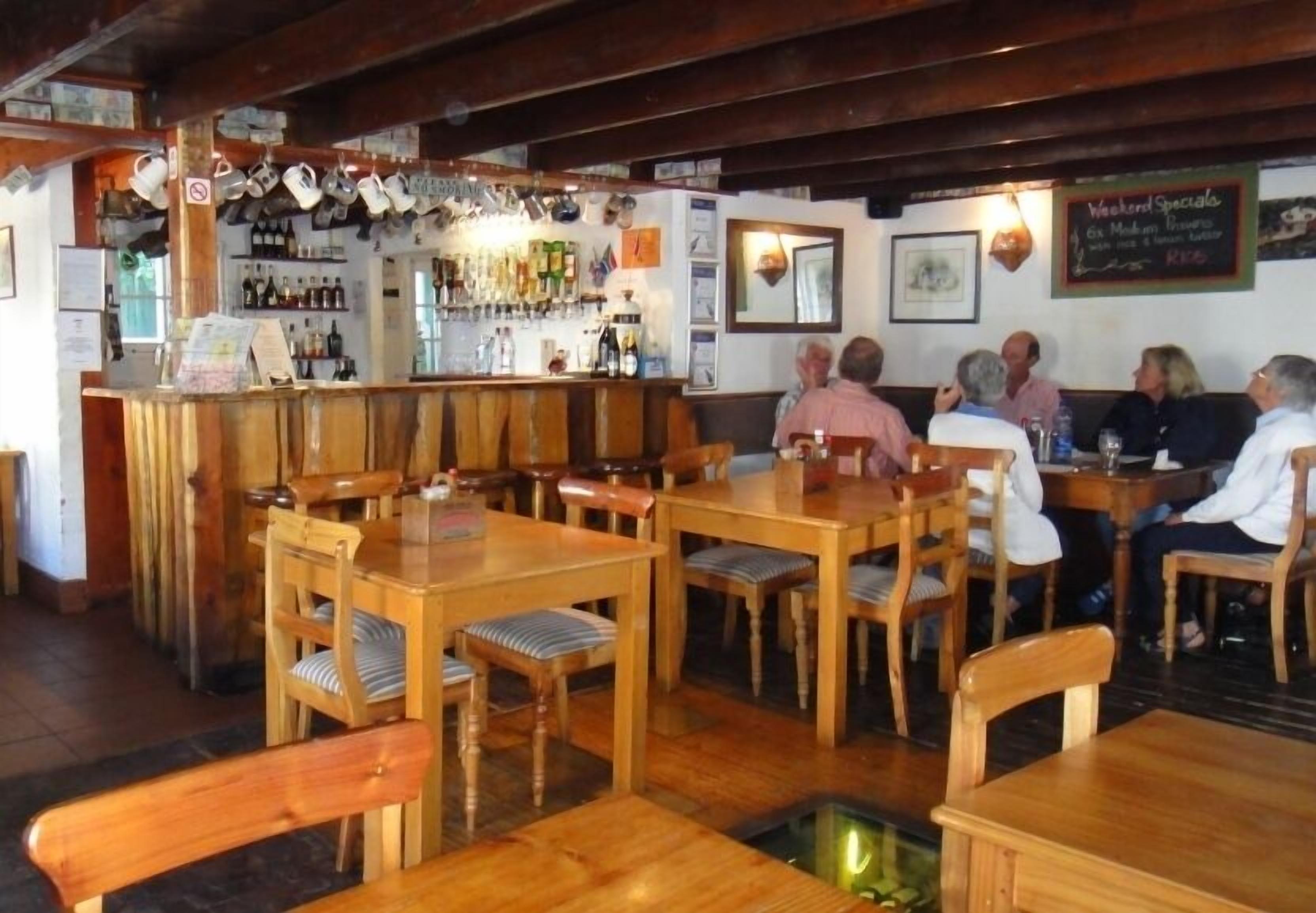 Un restaurant avec des tables et des chaises en bois, un bar avec des bouteilles et des verres, et un tableau affichant le menu sur le mur.