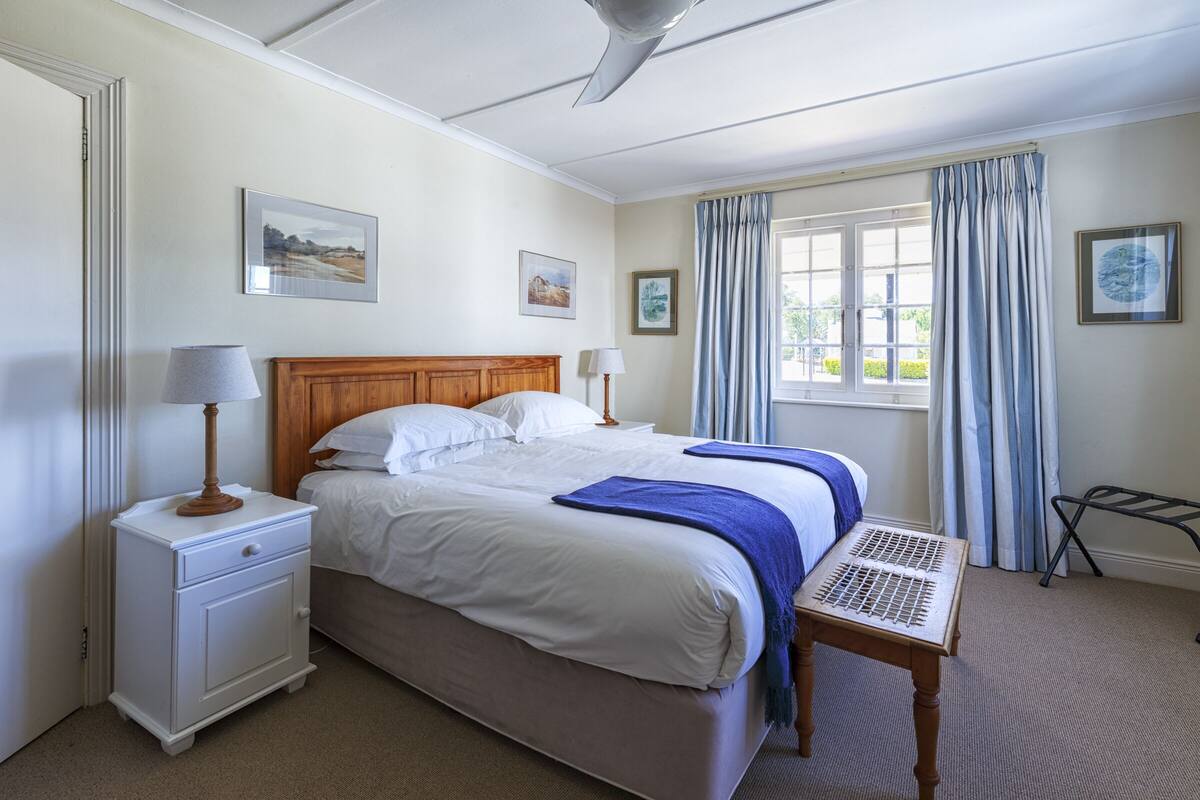A neatly arranged bedroom with a bed, bedside tables, a window with curtains, and wall-mounted artwork.