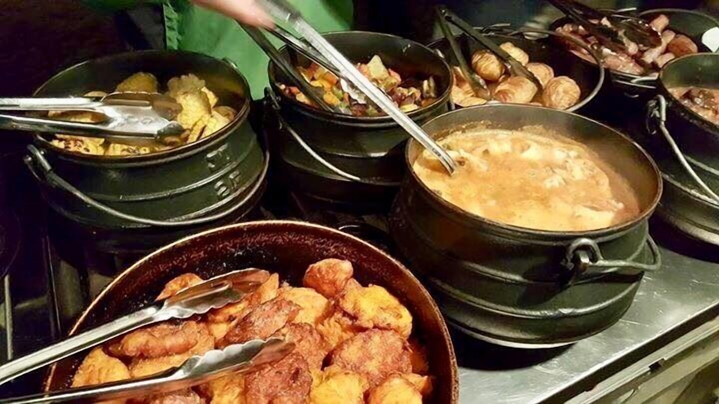 Buffet com diversos pratos em panelas e uma tigela de comidas fritas.