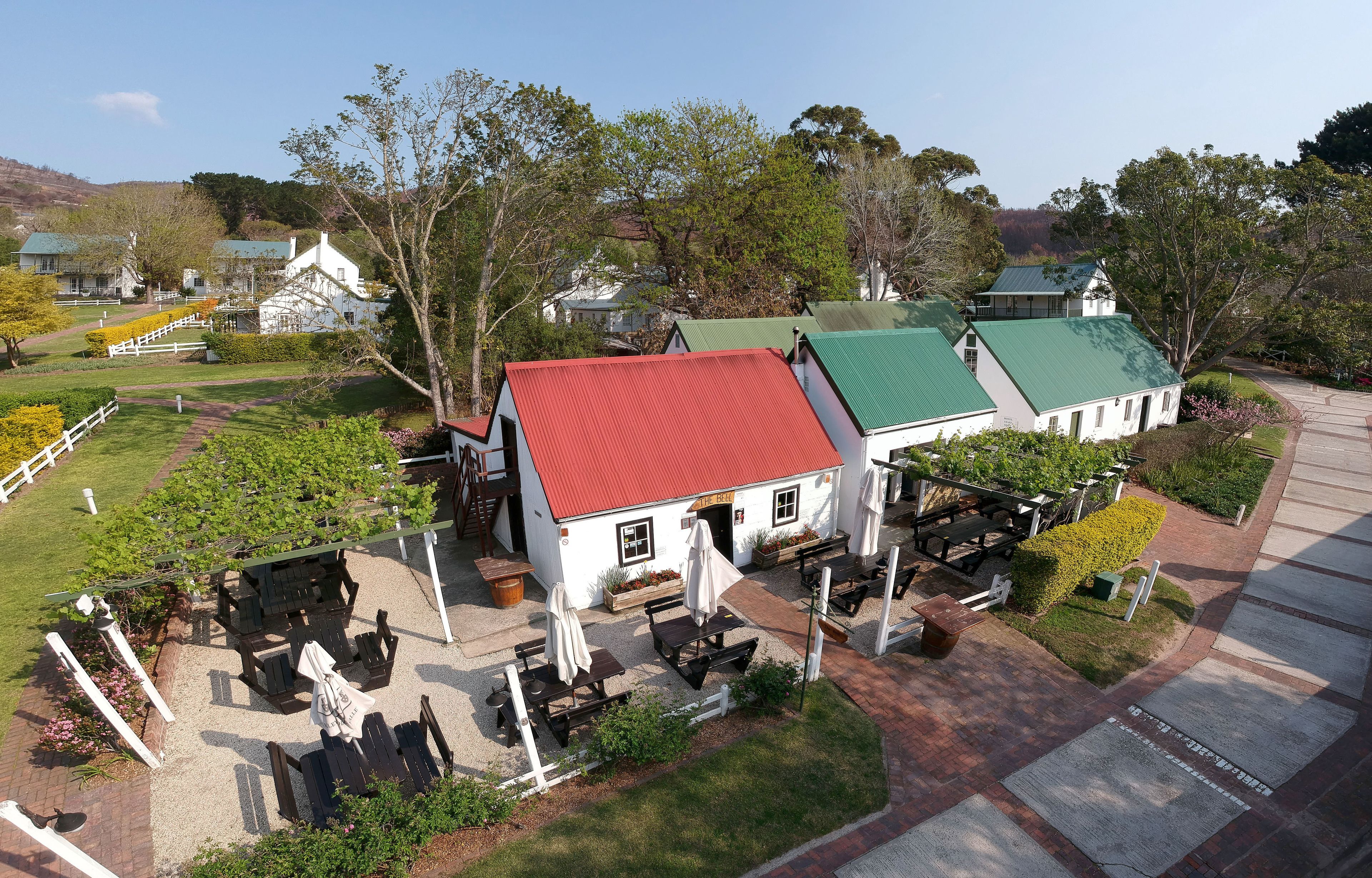 A white building with a red roof, surrounded by a well-maintained garden and outdoor seating area.
