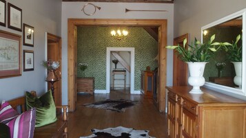 Un pasillo con piso de madera, alfombra de cuero, cuadros enmarcados, un candelabro y un espejo.