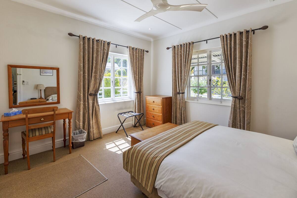 A bedroom with a bed, a desk, a chair, a dresser, and a window with curtains.