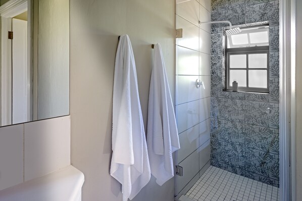 A bathroom with two white towels hanging on a wall-mounted rack, a glass shower enclosure with a window, and a toilet with a white seat.