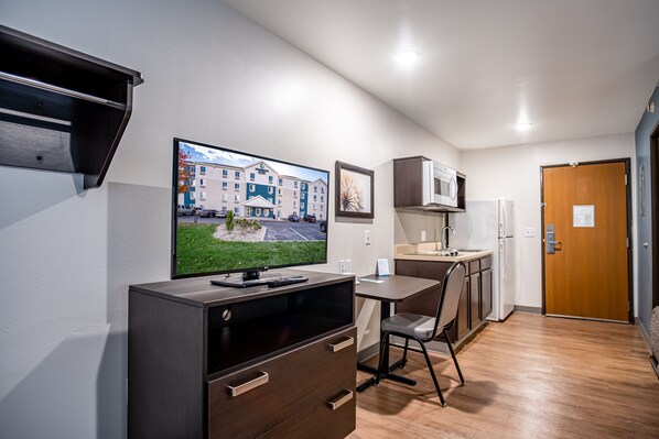 A compact kitchen with a flat-screen TV, a microwave, a refrigerator, and a wooden door. - WoodSpring Suites Columbus West - Hilliard (Columbus)