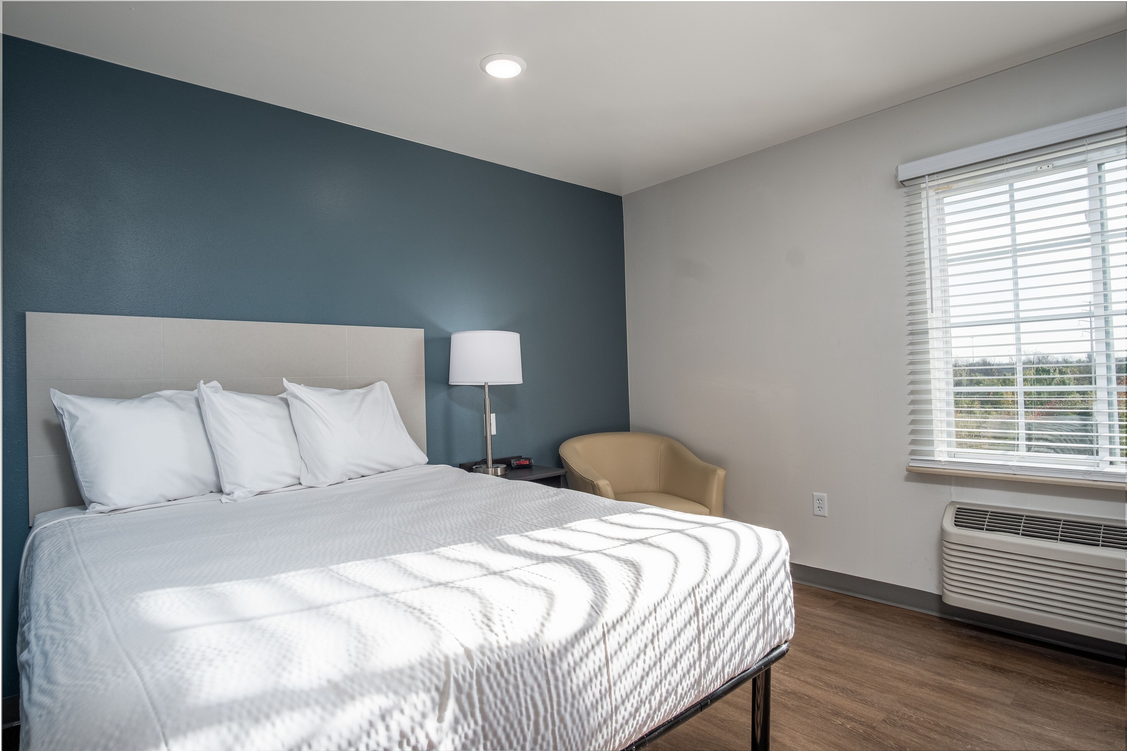 A hotel room with a bed, a chair, a lamp, and a window with blinds.