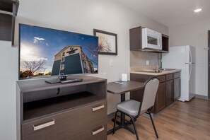 A compact kitchenette with a microwave, refrigerator, and a small countertop. A desk with a chair is positioned next to the kitchenette, and a flat-screen TV is mounted on the wall above the desk. - WoodSpring Suites Columbus West - Hilliard (Columbus)