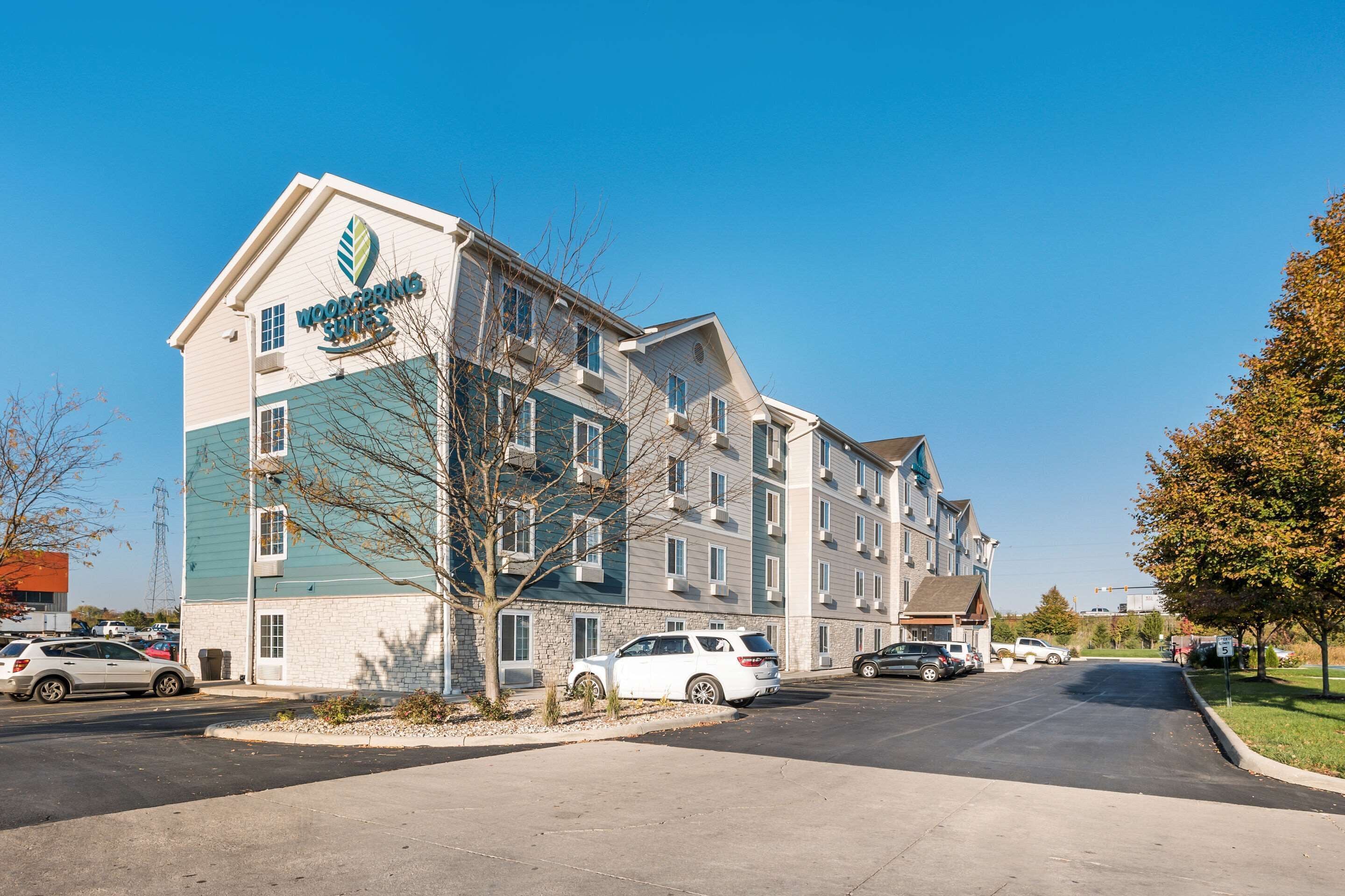 A multi-story hotel with a prominent 'Wyndham Suites' sign, a parking lot with several cars, and a clear blue sky.