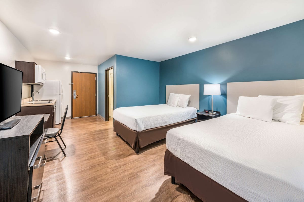 A hotel room with two beds, a desk with a TV, a chair, and a door.