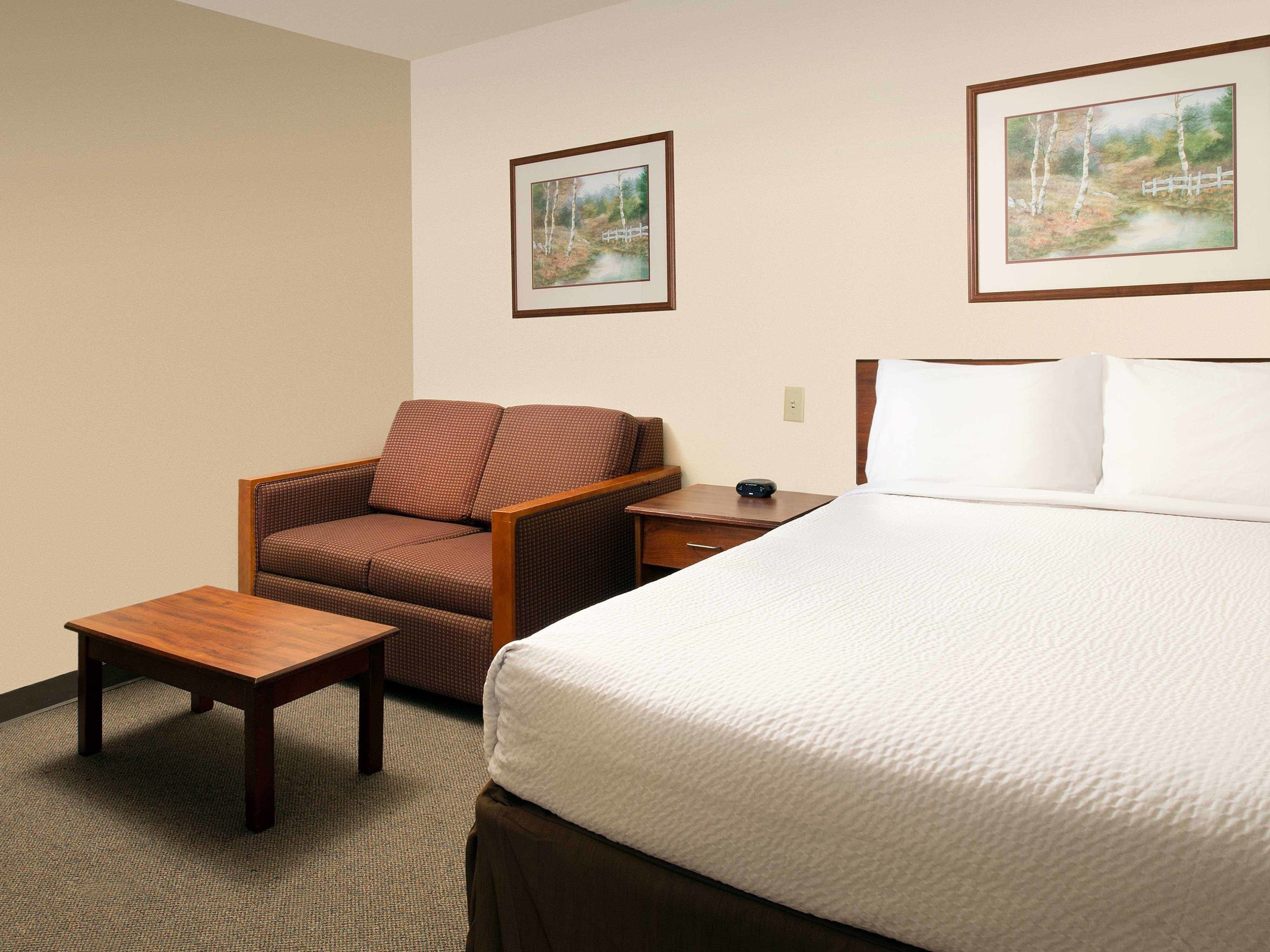 A hotel room with a bed, a chair, a nightstand, and two framed pictures on the wall.