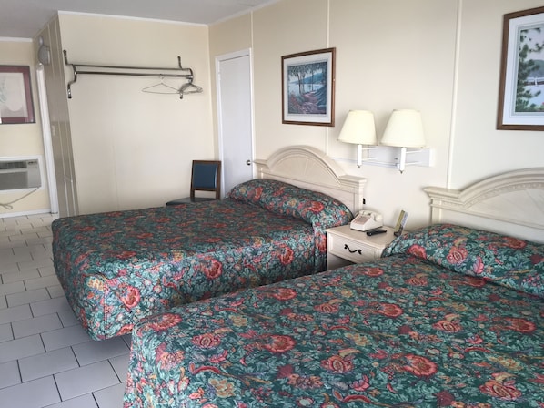 A hotel room with two beds, a nightstand with a phone and lamp, a door, and a wall-mounted towel rack.