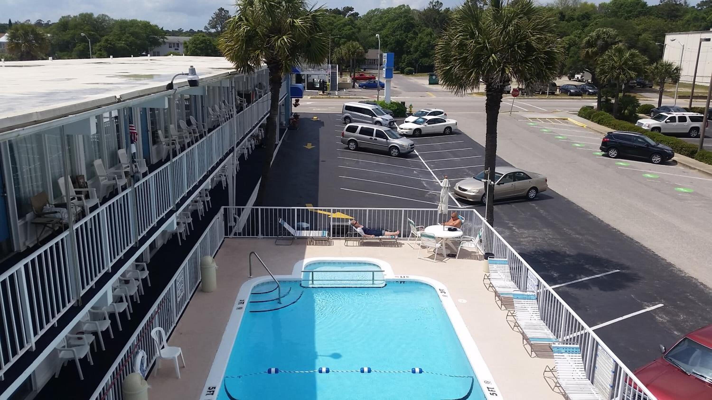 Area piscina con lettini e piscina, adiacente a un parcheggio con auto e un segnale di stop.