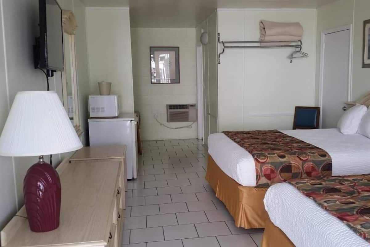 Quarto de hotel com duas camas, uma escrivaninha com luminária, micro-ondas, mini-geladeira, janela e porta-toalhas.