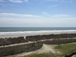 A beach with a sandy path leading to the water, a wooden fence, and a clear sky.
