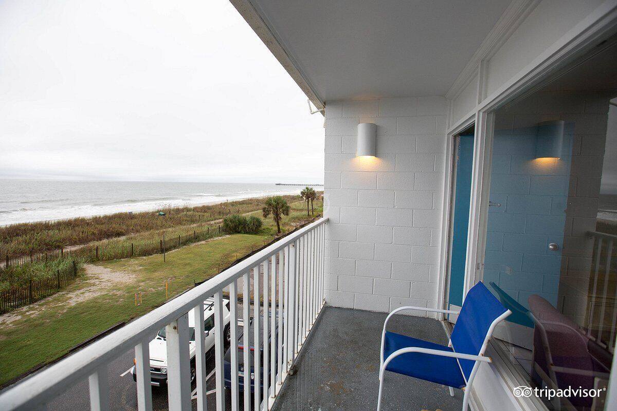 Varanda com vista para a praia, corrimão branco, cadeira azul e porta com moldura azul.