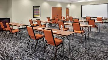 A conference room with multiple tables and chairs, equipped with water bottles, a projector screen, and a carpeted floor.