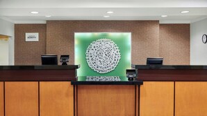 A hotel reception desk with a modern design, a nameplate, a decorative wall piece, and a clock on the wall. - Fairfield Inn & Suites by Marriott Cartersville (Cartersville)