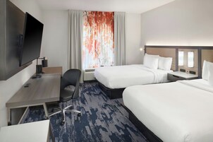 Habitación de hotel con dos camas, un escritorio con silla, un televisor de pantalla plana y una ventana con cortinas.