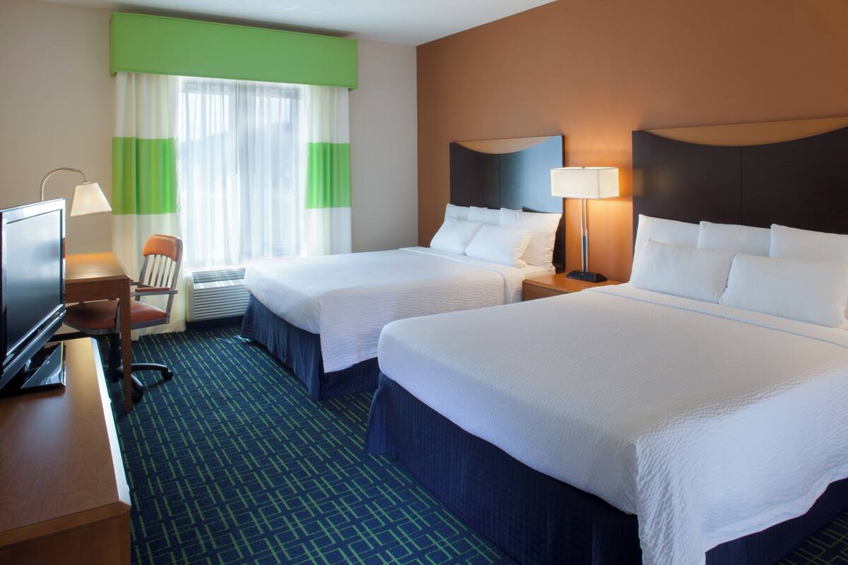 A hotel room with two beds, a desk with a computer, a chair, and a window with curtains.