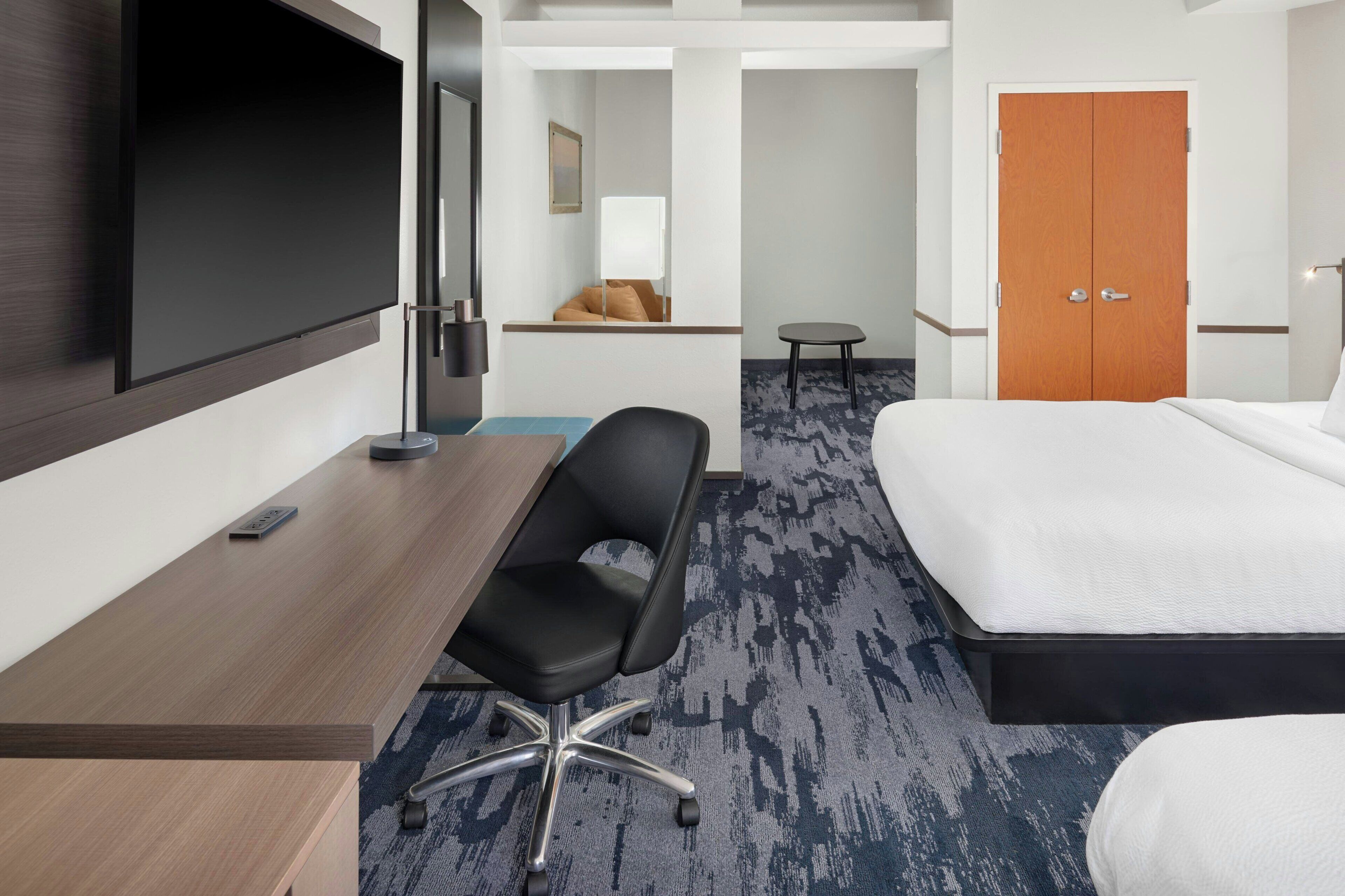 A hotel room with a bed, a desk, a chair, a TV, and a door.