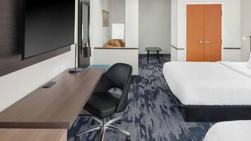 A hotel room with a bed, a desk, a chair, a TV, and a door.