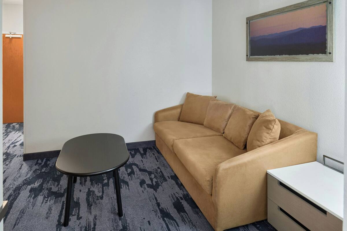 A room with a beige sofa, a small black table, and a white nightstand.