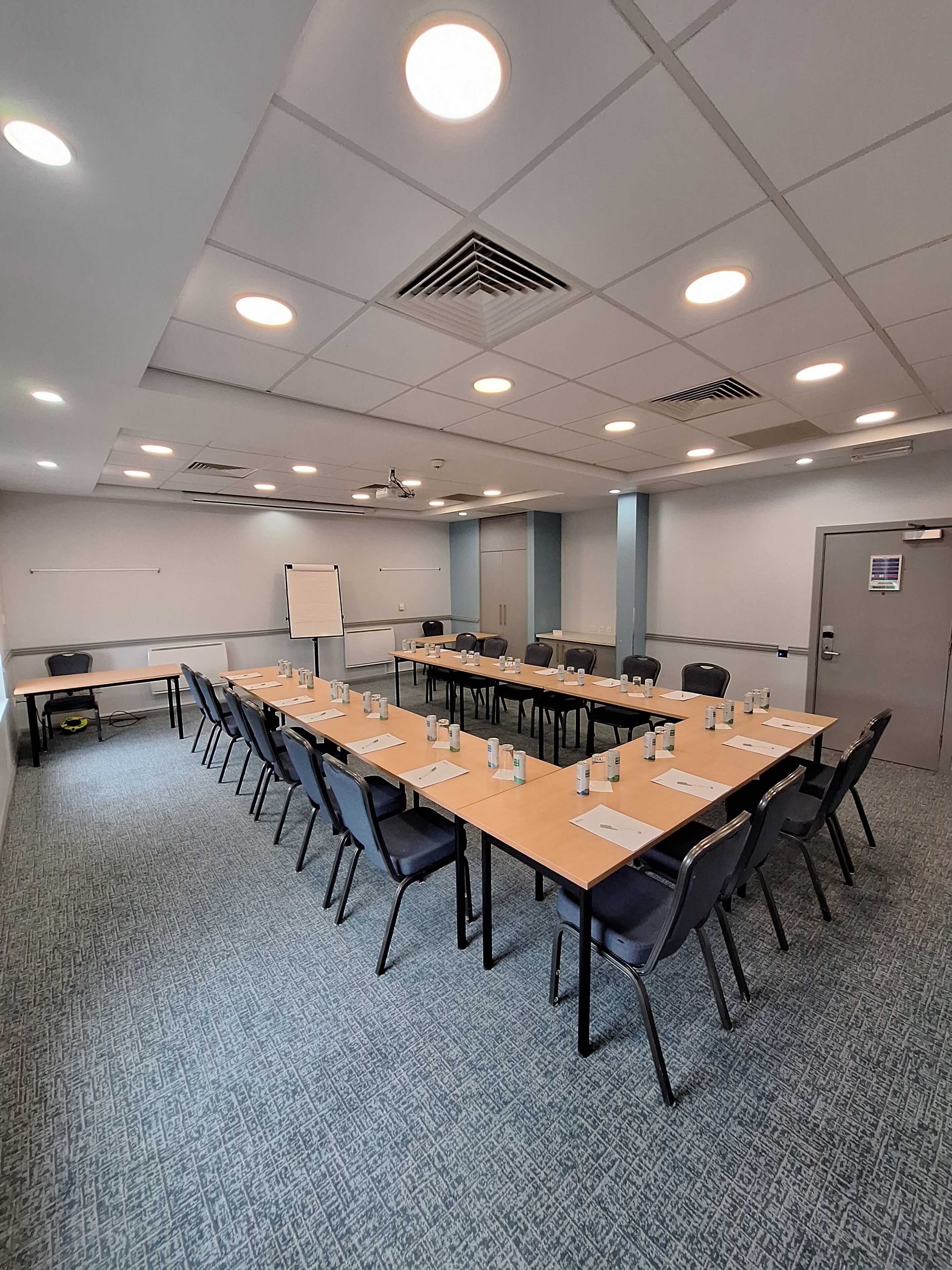 Un salón de conferencias con una larga mesa, sillas, una pizarra y una pantalla para proyector.