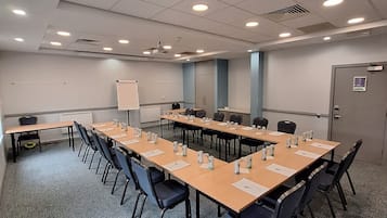 Un salón de conferencias con una larga mesa, sillas, una pizarra y una pantalla para proyector.