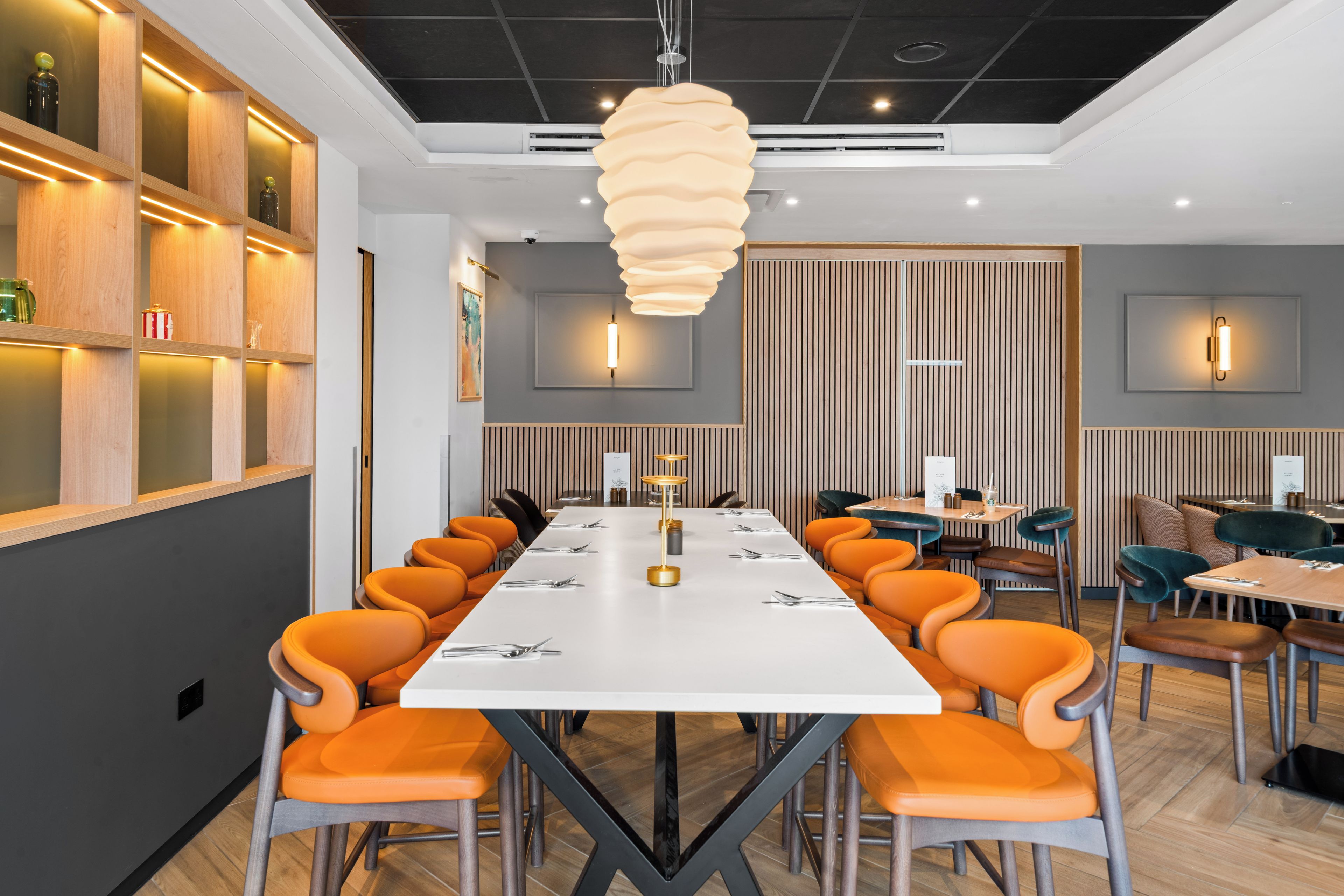 Ett modernt konferensrum med ett långt bord, orange stolar och en unik hänglampa.