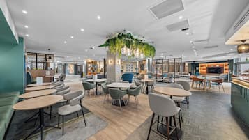 Ein modernes Café mit runden Tischen, Stühlen und einer hängenden Pflanze in der Mitte.