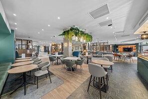A modern cafe with round tables, chairs, and a central hanging plant.