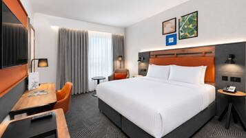 A hotel room with a large bed, a desk with a chair, a TV, and a small table.