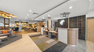 Un moderno vestíbulo de hotel con mostrador de recepción, zona de estar y un bar/lounge al fondo.
