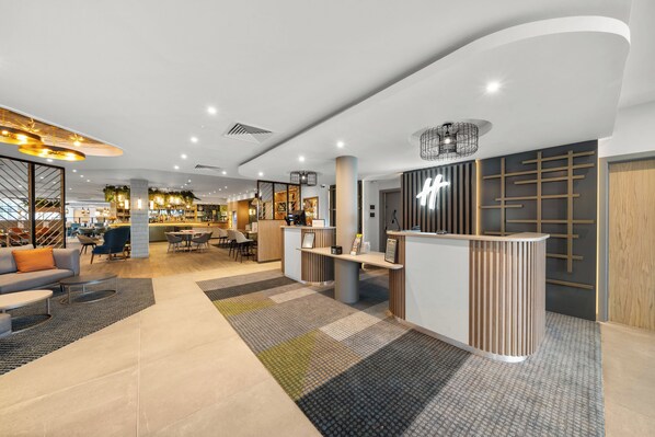 A modern hotel lobby with a reception desk, seating area, and a bar/lounge in the background. - Holiday Inn London Luton North by IHG (Luton)