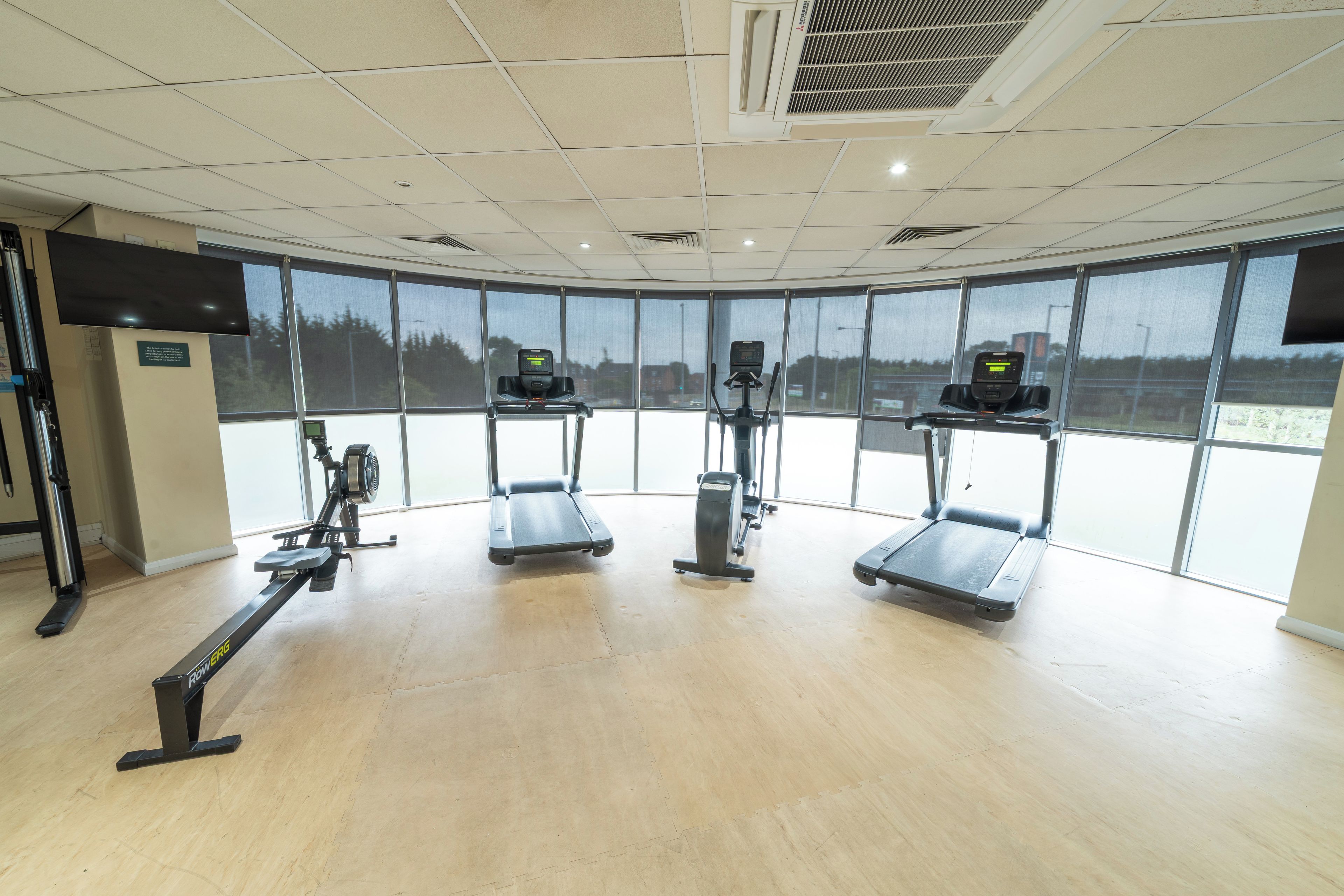 A gym with exercise equipment, large windows, and a ceiling with air conditioning vents.