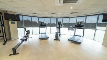 A gym with exercise equipment, large windows, and a ceiling with air conditioning vents.
