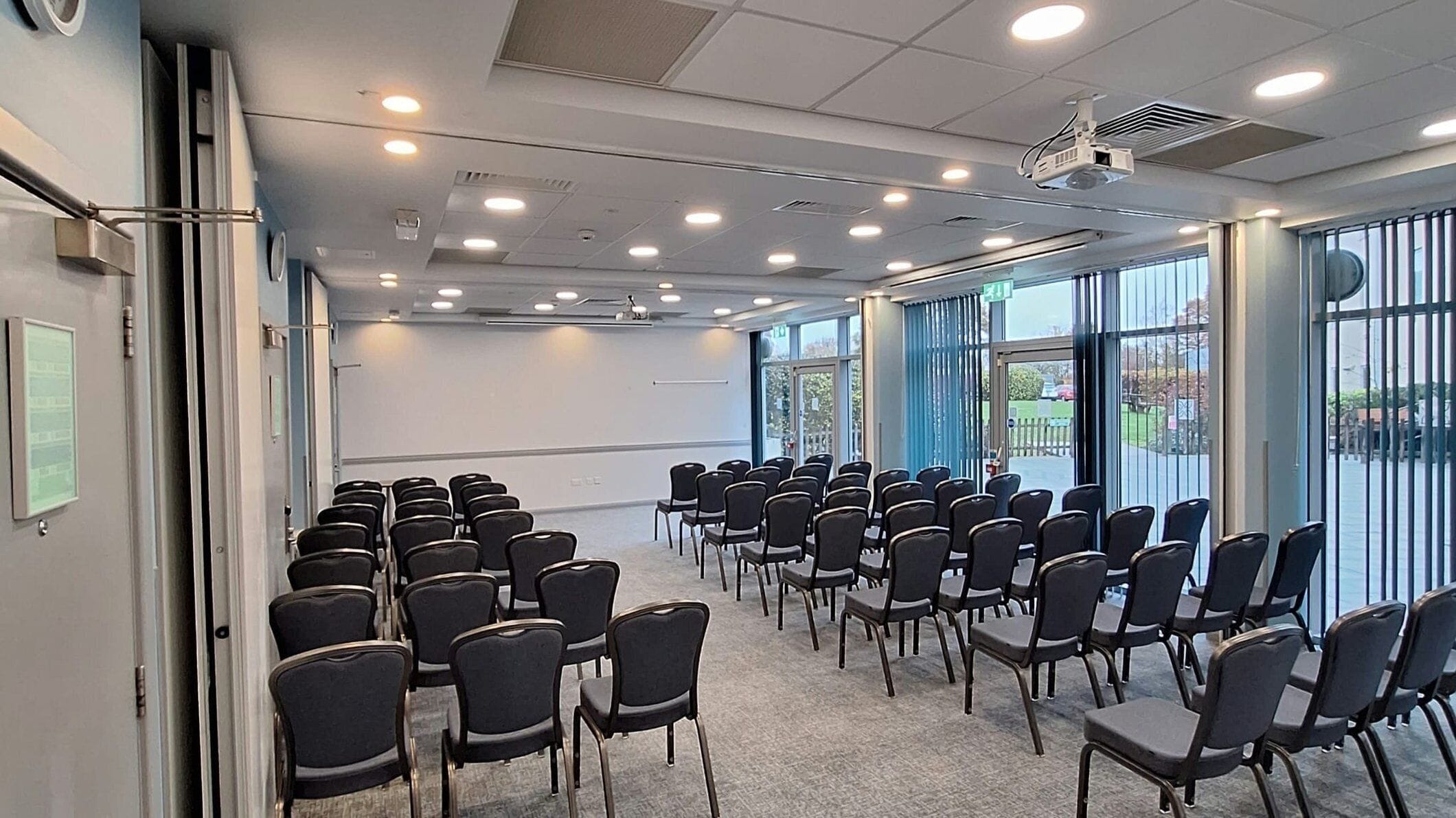 Une salle de conférence avec des rangées de chaises, un projecteur et de grandes fenêtres.
