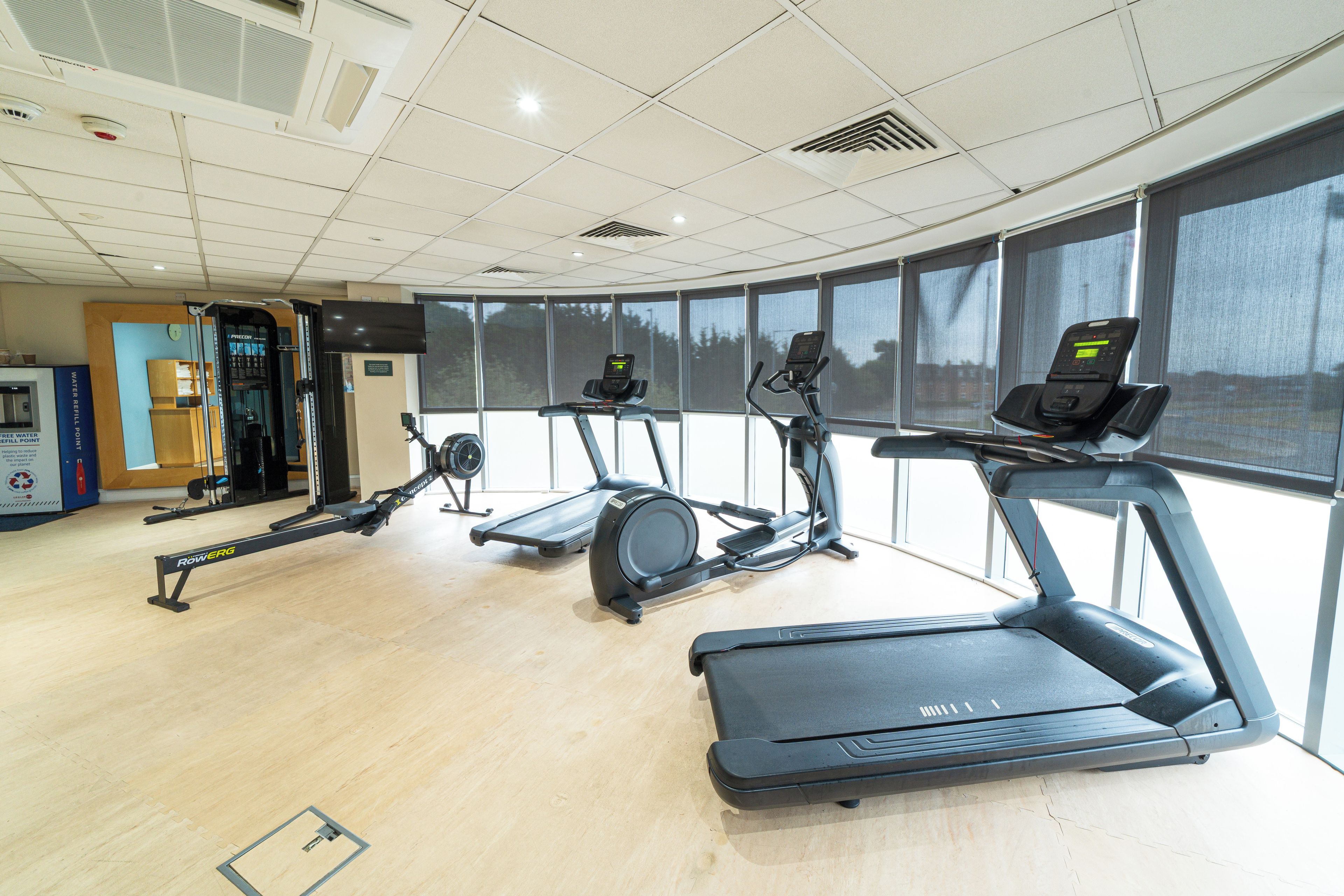 Un gimnasio con varios equipos de ejercicio, incluyendo cintas de correr, una elíptica y una máquina de remo.